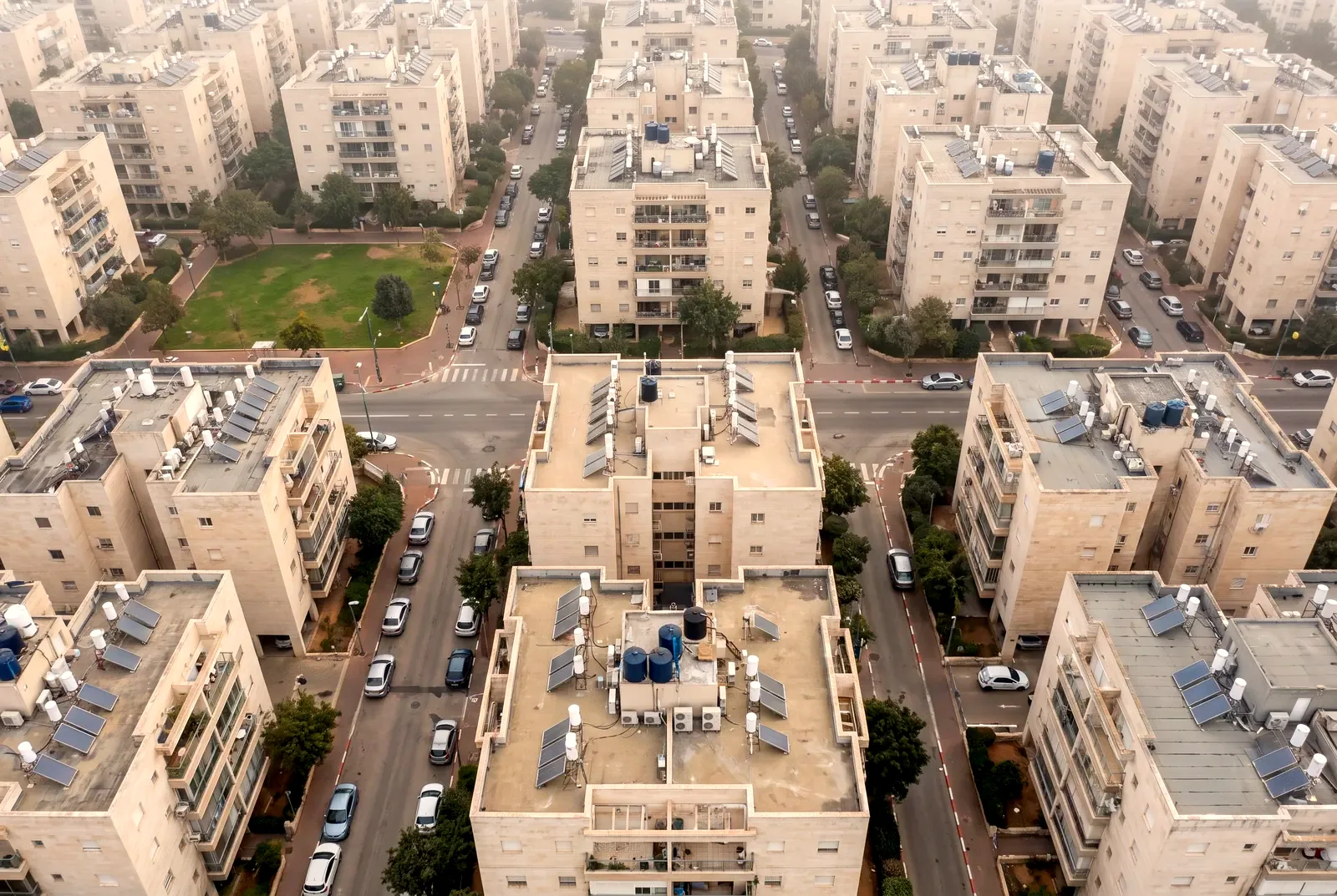 הדמיה: צילום מהאוויר ישר מלמעלה של גגות בנייני דירות עם דודי שמש ורחובות מוצלים בעצים