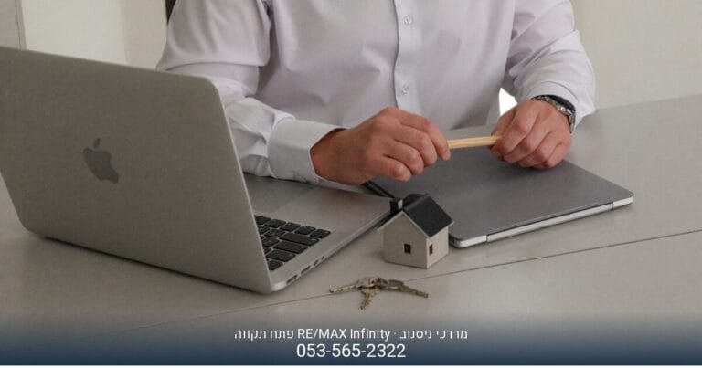 מרדכי ניסנוב מ-RE/MAX Infinity פתח תקווה, יושב ליד שולחן עם מחשב נייד וטלפון