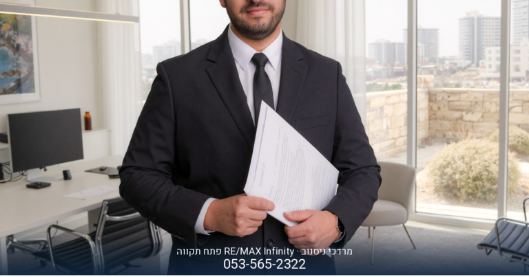 מרדכי ניסנוב, מתווך RE/MAX בפתח תקווה, עומד בחליפה ליד מסך מחשב